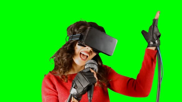 A girl wearing a virtual reality headset and wired gloves, singing with a microphone. Pre-keyed chroma-key shot.