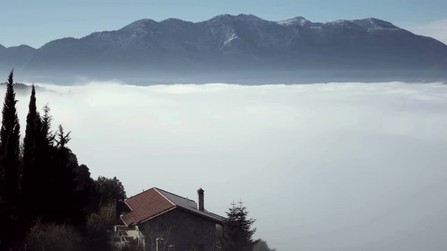 4K rural house on edge of cliff, fog,morning, mountain view.A traditional mountain cabin/house on the edge of a cliff overseeing a beautiful Greek rural landscape with mountains on the horizon