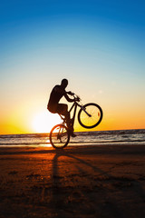 Naklejka na ściany i meble Man cyclist silhouette on blue sky and multicolored sunset backg