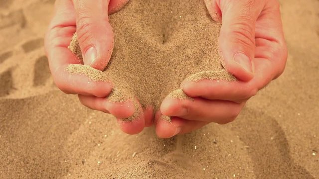 Handful of sand pouring through fingers, sand dust flowing as time passes.