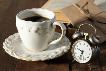 silver wind-up alarm clock on a wooden table with a Cup of coffee and a book