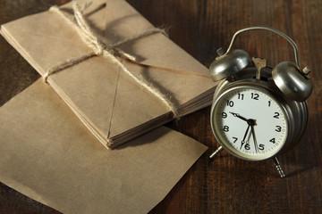 silver wind-up alarm clock on a wooden table with a bunch of letters