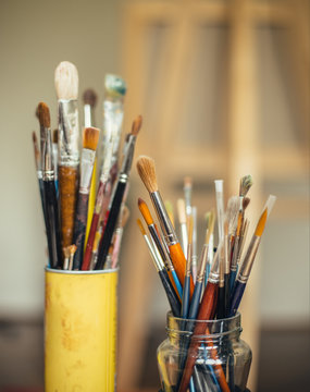 Paintbrushes in two jars with easel in background