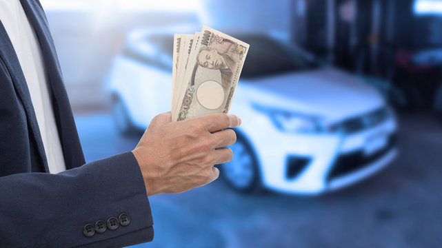 Businessman hand holding Japanese banknote with blur car backgro - Powered by Adobe