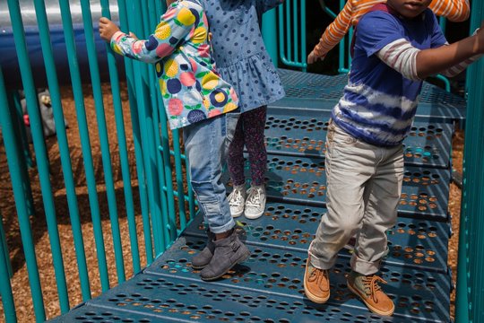 Cropped shot of four boys and girls playing on climbing frame in playground