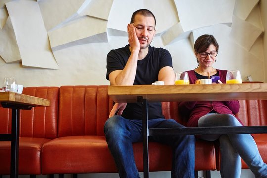 Bored man with girlfriend reading smartphone text in restaurant