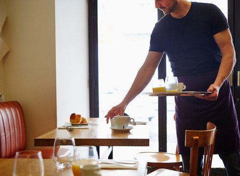 Waiter Clearing Table In Restaurant