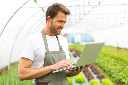 Portrait of an attractive farmer in a greenhouse using laptop