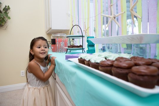 Young girl looking longingly at cakes on kitchen work surface