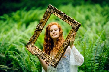 Young woman holding gold picture frame  amongst  forest ferns