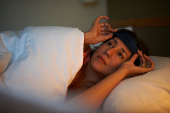 Mature woman putting on eye mask in hotel bed at night