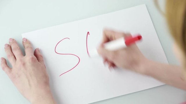 Female hands holding pen and blank paper sheets with copyspace on table. He writes the word SOS