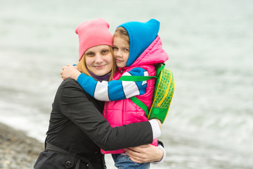 Mom and daughter in warm clothing standing arm in arm on the beach
