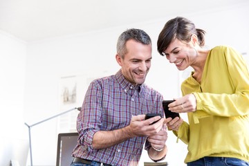 Low angle view of colleagues in office looking at smartphones smiling
