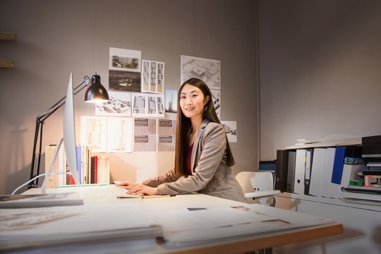 Side view of mid adult woman at desk using computer looking at camera smiling