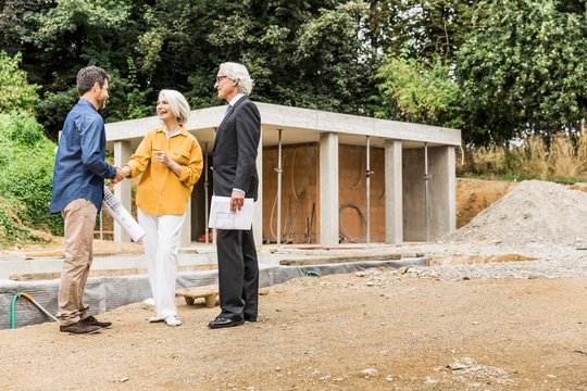Couple on construction site shaking hands with architect smiling