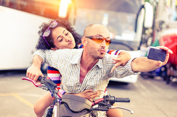 Couple of bikers taking funny selfie riding motorbike on urban traffic road at sunset - Concept of...