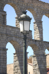 In the foreground a streetlamp, at the background (out of focus) the ancient roman aqueduct located in Segovia, Castile and Leon, Spain