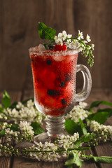 Berry soft drink with ice on a wooden background and flowers