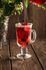 Berry soft drink with ice on a wooden background and flowers