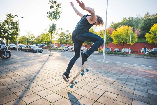Young male urban skateboarder doing skateboarding jump trick on sidewalk