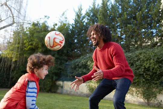 Father and son playing with football in garden smiling