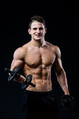 Fototapeta na wymiar Handsome power athletic man training pumping up muscles with dumbbells in a gym. Fitness muscular body isolated on black background. Looking to the camera.