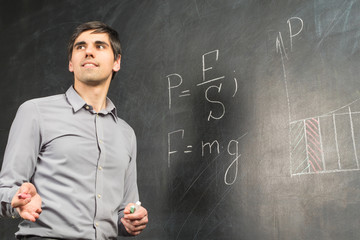 Portrait of young happy smiling teacher man standing near chalkboard with mathematical formulas and...