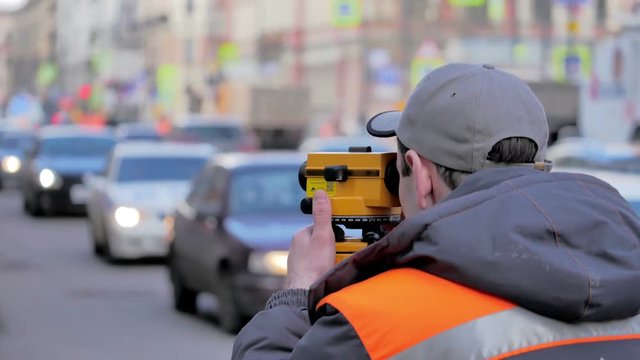 Engineers use tacheometer or theodolite for survey line in city centre, on a background of road works