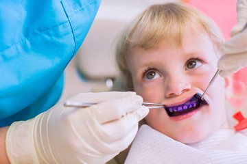 Girl with plaque disclosing tablet on teeth having dental examination