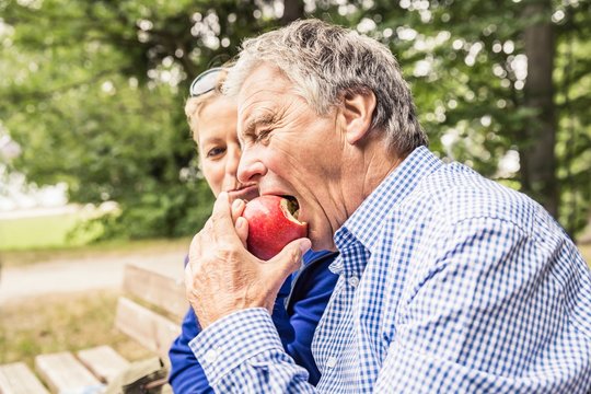 Couple sitting outdoors, mature woman sharing apple