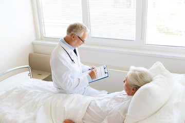 senior woman and doctor with clipboard at hospital