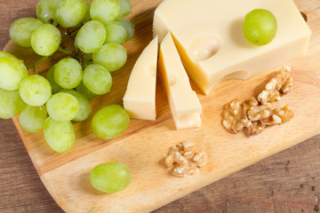 Cheese with brush of grapes and walnuts on a wooden table