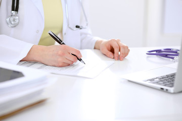 Close-up of a female doctor filling  out application form , sitting at the table in the hospital