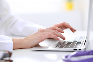 Close-up of female doctor typing laptop sitting at a table in the hospital