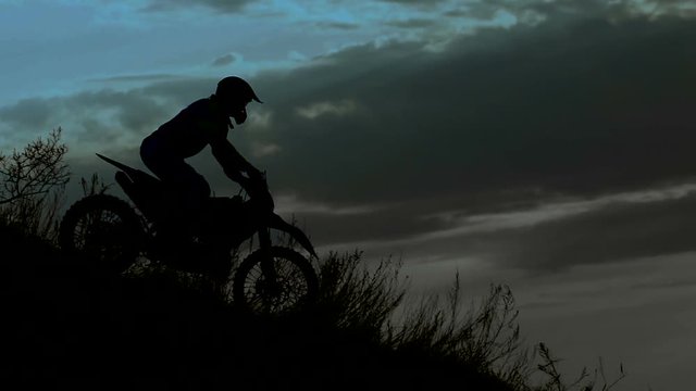 Rider silhouette in the night. He goes down the hill on his extreme motocross bike. 