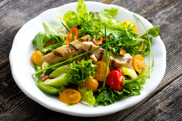 Delicious salad with grilled chicken breast on a wooden background