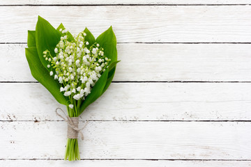 Blumenstrauß aus Maiglöckchen mit grünen Blättern, die mit Bindfäden in den Wassertropfen auf den weißen Holzbrettern gebunden sind. mit Platz zum Posten von Informationen