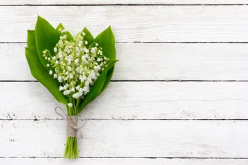 Fototapete Maiglöckchen Blumenstrauß aus Maiglöckchen mit grünen Blättern, die mit Bindfäden in den Wassertropfen auf den weißen Holzbrettern gebunden sind. mit Platz zum Posten von Informationen