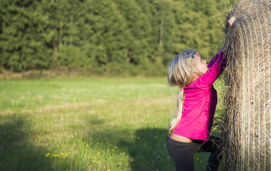 Obraz premium Child blond Girl by straw hay bale in field, meadow, smiling, playing, portrait, summer, nature