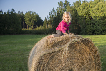Naklejka na ściany i meble Child blond Girl by straw hay bale in field, meadow, smiling, playing, portrait, summer, nature