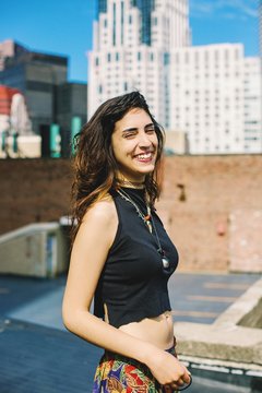 Side view of woman with nose ring on rooftop wearing crop top looking at camera eyes closed, smiling, Boston, Massachusetts, USA