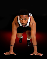 Male track runner in starting position.  Isolated on black background with red flare highlights on floor.