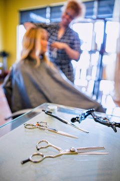 Stylist cutting woman's hair in hair salon, focus on scissors in foreground