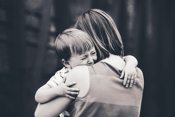 Black and white portrait of  young Caucasian woman mother comforting her crying little toddler boy...