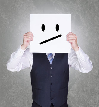 Gesch&auml;ftsmann h&auml;lt sich Schild mit genervtem Smiley vor sein Gesicht
