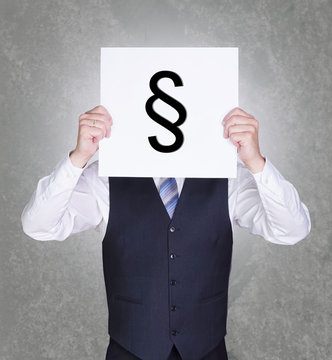 Gesch&auml;ftsmann h&auml;lt sich Schild mit Paragraphensymbol vor sein Gesicht