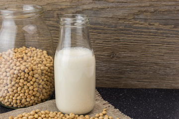 Soybeans and bottle of soy milk, on wooden background.
