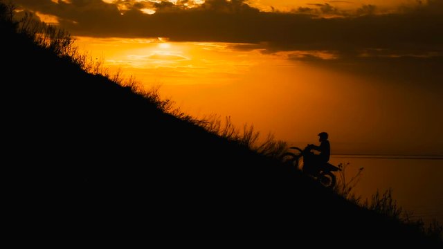 motocross rider storms obstacle. Climb up the hill on the road. Sunset painted the sky 