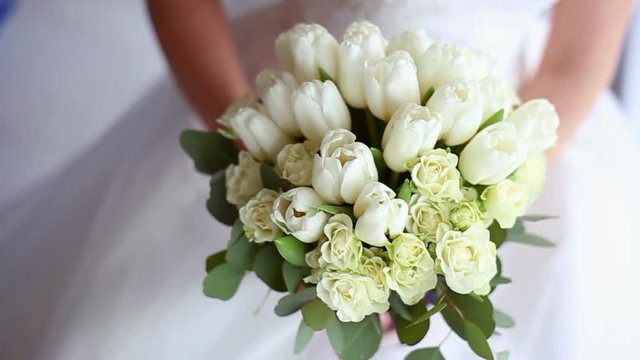 Beautiful bridal bouquet in hands of young bride dressed in white wedding dress. Close up of big bunch of fresh white roses and tulips flowers in female hands. Anonymous bride holding flowers.
